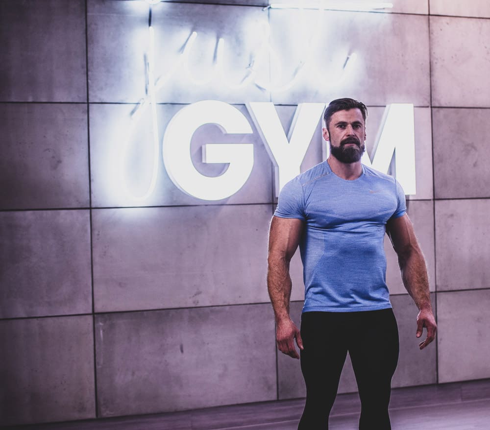 Tomasz Bigus na tle neonu siłowni JustGYM w Olsztynie